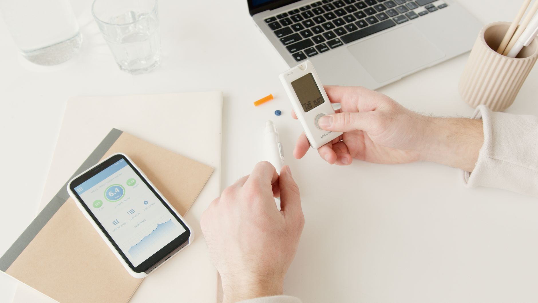 Bureau clair vu du dessus : un smartphone posé sur un carnet beige, à côté d’un verre d’eau.